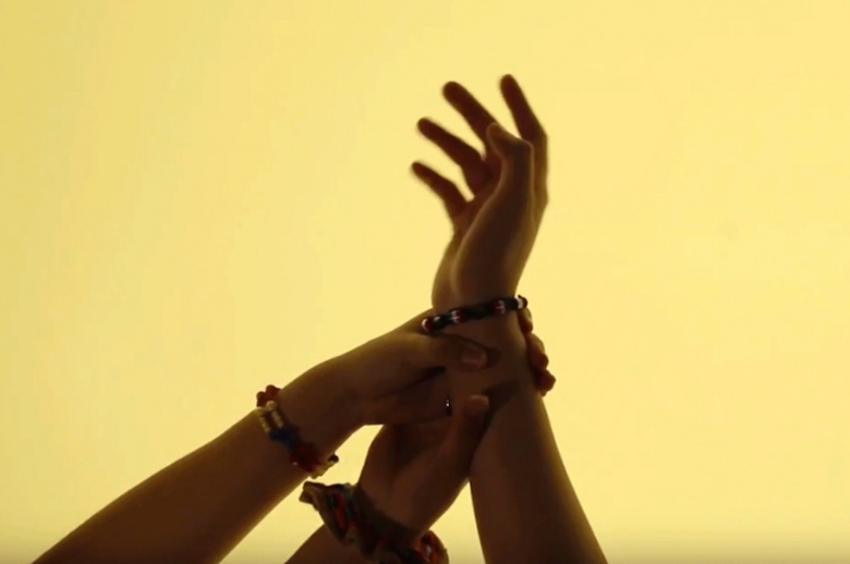 Three hands lifted and grasping each other, against a yellow backdrop